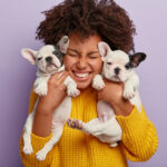 close-up-shot-pleased-woman-with-afro-hair-holds-two-puppies-spends-leisure-time-with-loyal-animal-friends-happy-have-newborn-french-bulldog-dogs (1)